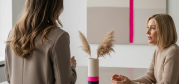 Zwei Frauen in einem modernen Studio im Gespräch, dezente Beige- und Taupetöne mit Akzenten in Neonmagenta, symbolisch für strategisches Markenbranding.